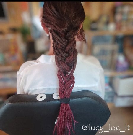 a girl in the hair salon with burgundy dreads weaved in a braid 